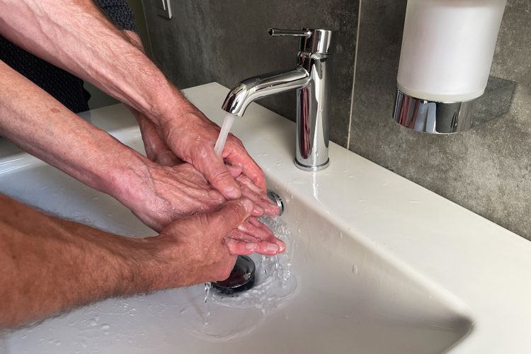 Grundpflege Zwei Hände waschen zwei ältere Hände unter einem Wasserhahn in einem Waschbecken.